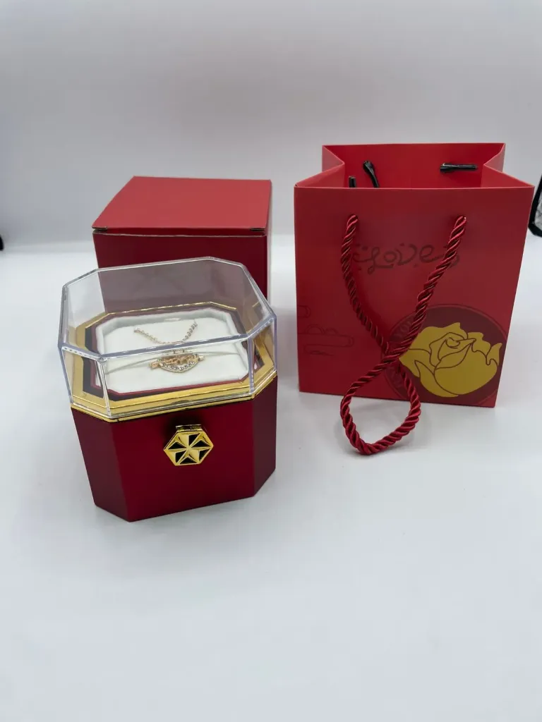 Rotating preserved rose gift box set.  It includes a preserved red rose housed in an octagonal, clear-top box with a hidden compartment that  contains a necklace
