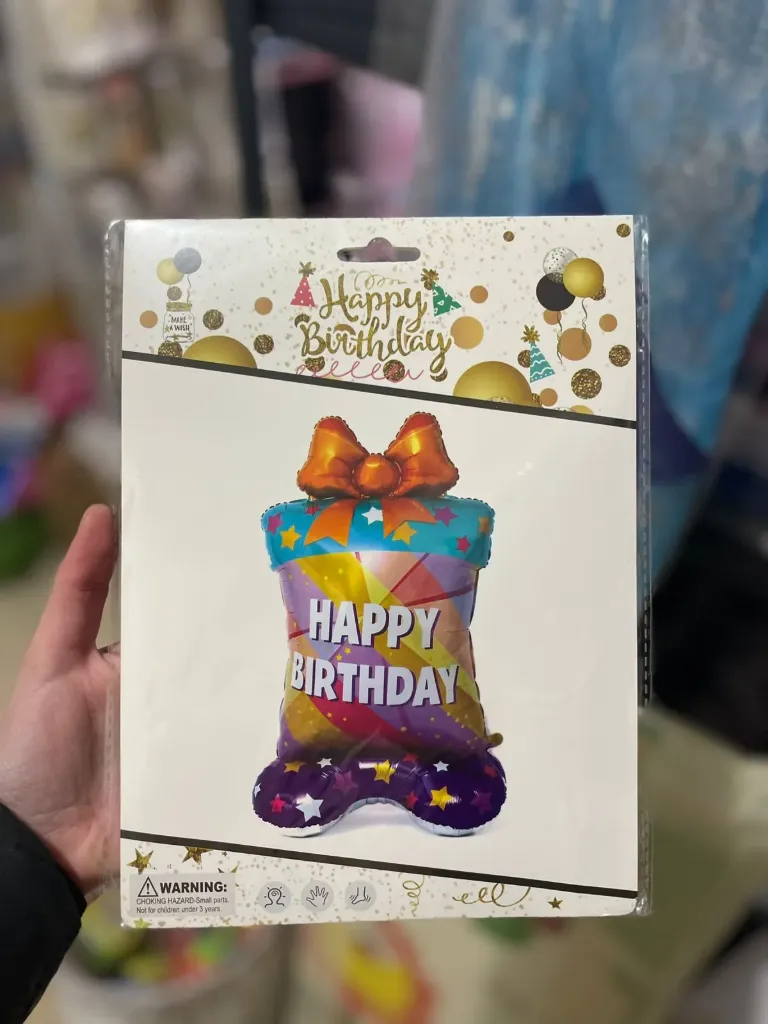Free-standing birthday  foil balloon 120cm  shiny, multi-colored design resembling a wrapped gift with a bow on top and "HAPPY BIRTHDAY"