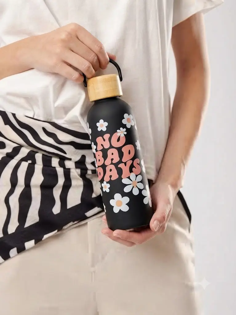 Double-wall insulated stainless steel water bottle featuring white daisy floral patterns and  "NO BAD DAYS". It is equipped with a natural wooden screw-on lid and a convenient carrying strap